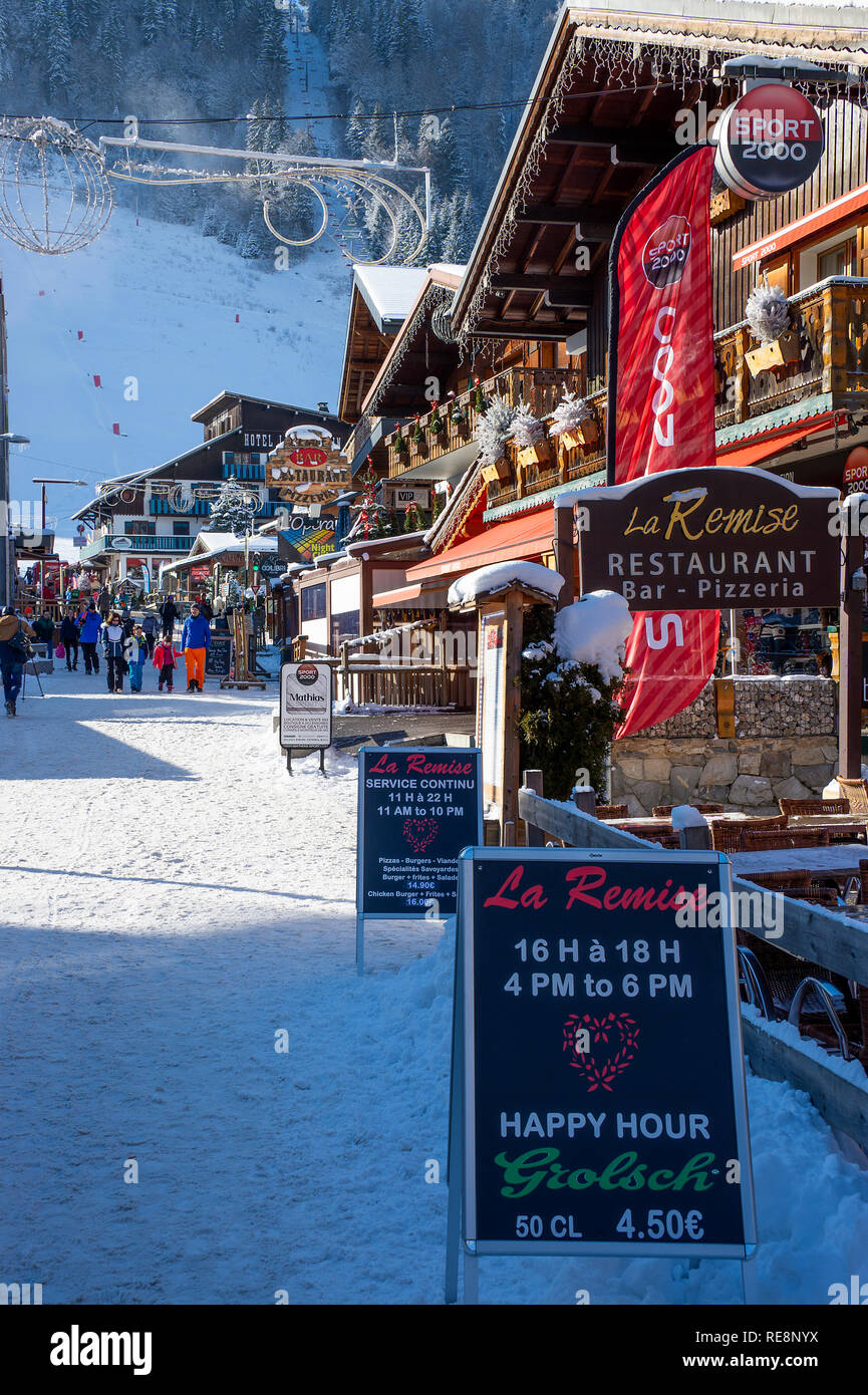 Colourful Shops and Restaurants with Ski Slopes Behind and Snow Covered Street in Morzine Haute Savoie Portes du Soleil France Stock Photo