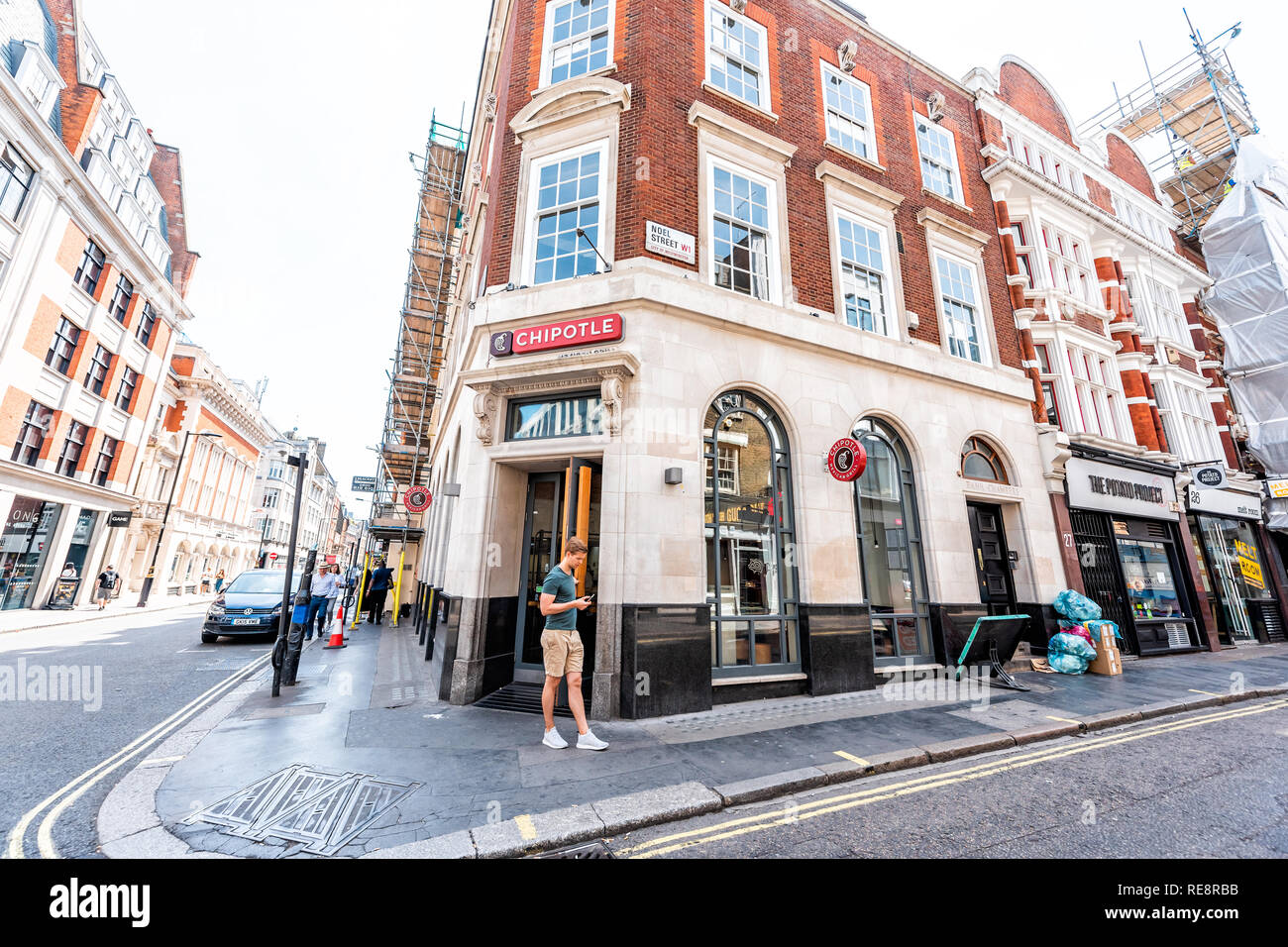 London, UK - June 24, 2018: Chipotle restaurant fast food store shop with man standing by entrance exterior in Soho with sign on historic brick buildi Stock Photo