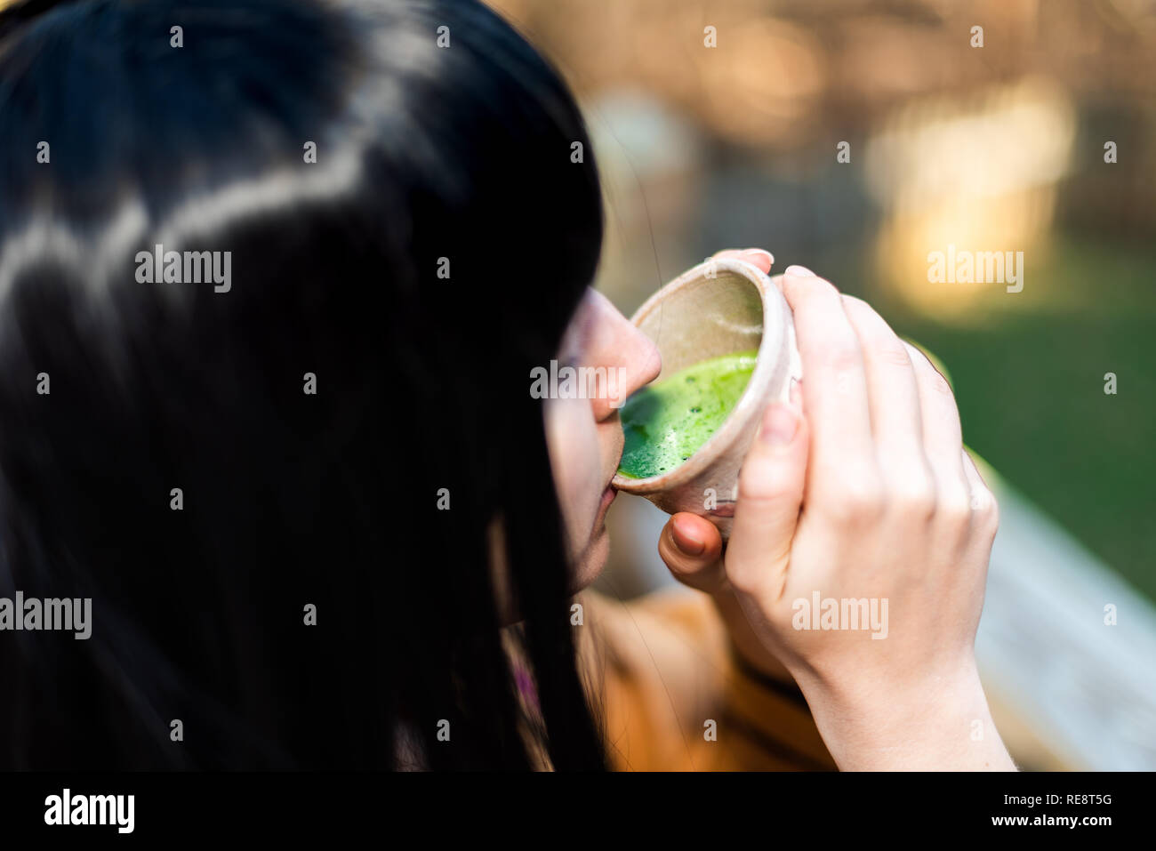 Woman holding tea cup face closeup drinking outside in backyard garden with girl and green matcha black hair Stock Photo