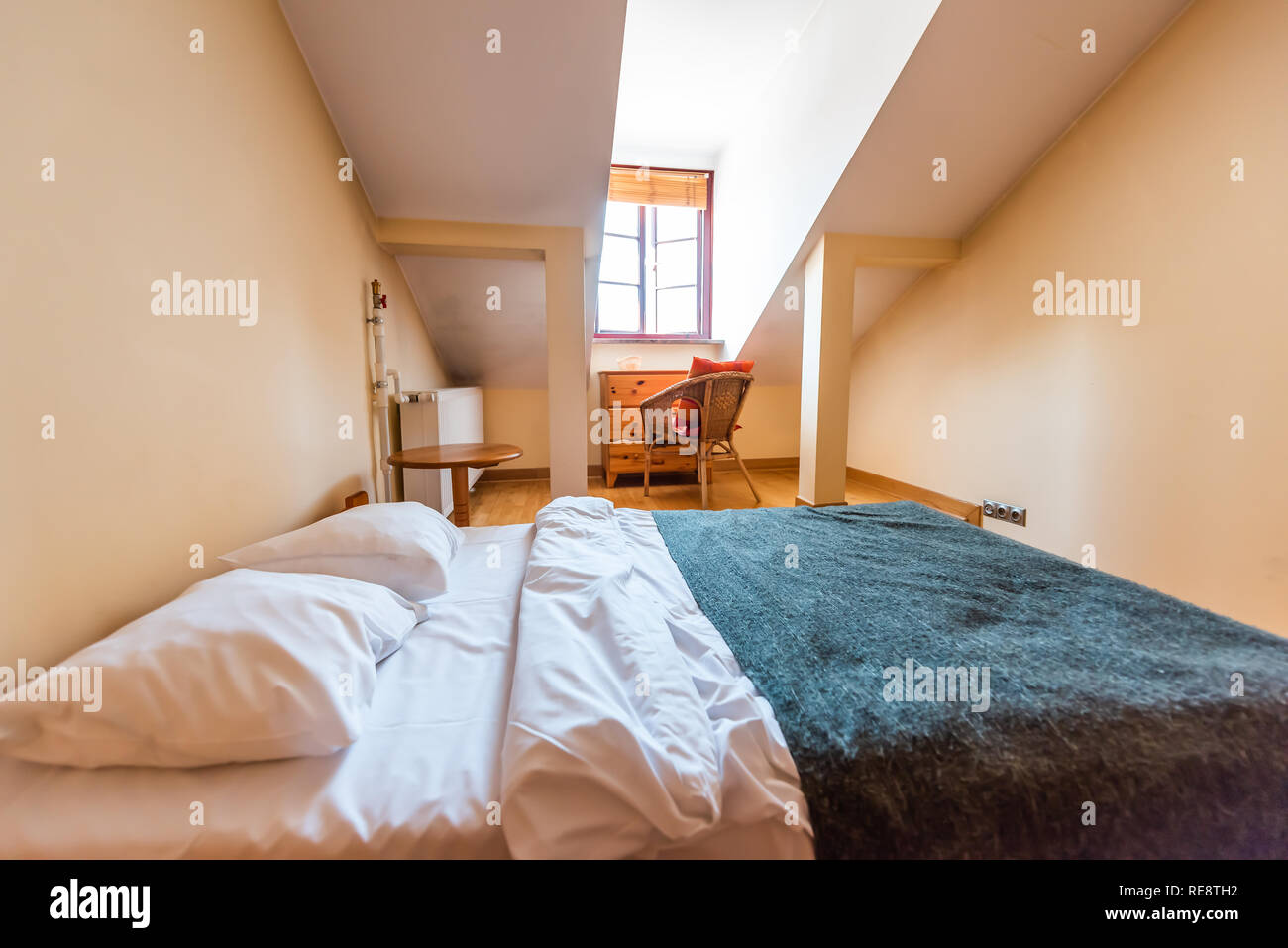 New clean European double queen bed with slanted ceiling and window in