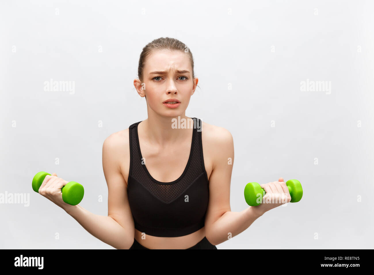 Sad Caucasian young woman with long medium brown hair in casual outfit holding dumbbell - Isolated Stock Photo