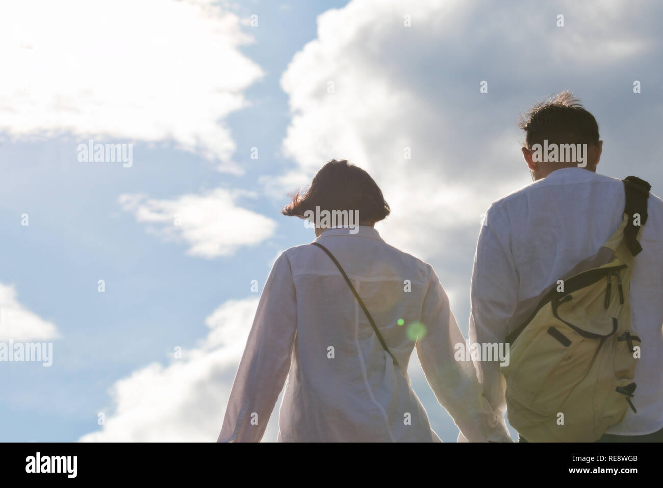 young couple holding hands against blue sky with clouds Stock Photo - Alamy