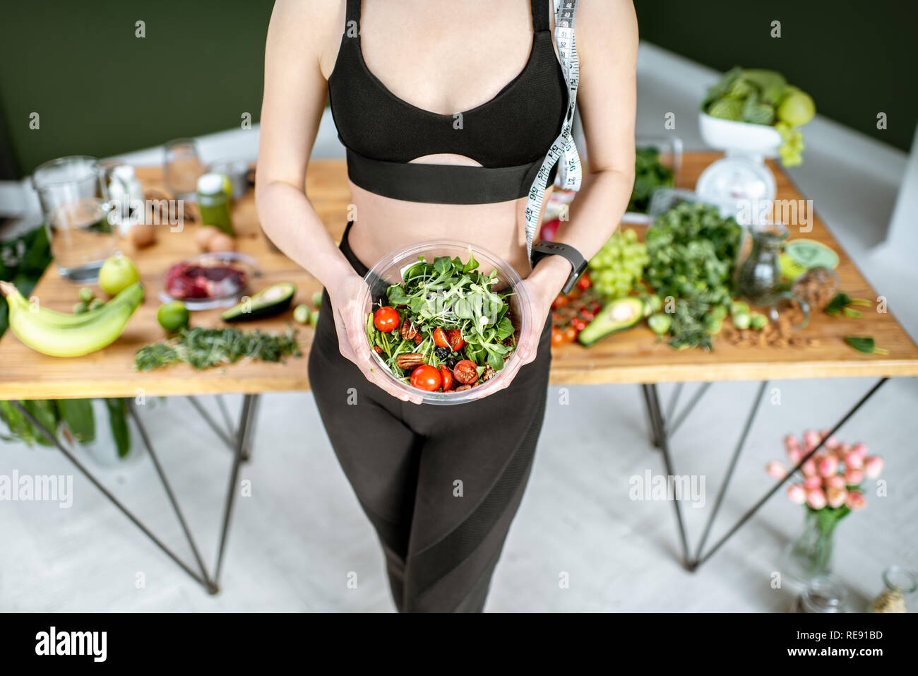 Athletic woman in sportswear holding salad near the table full of healthy products. Healthy eating and sports lifestyle concept Stock Photo