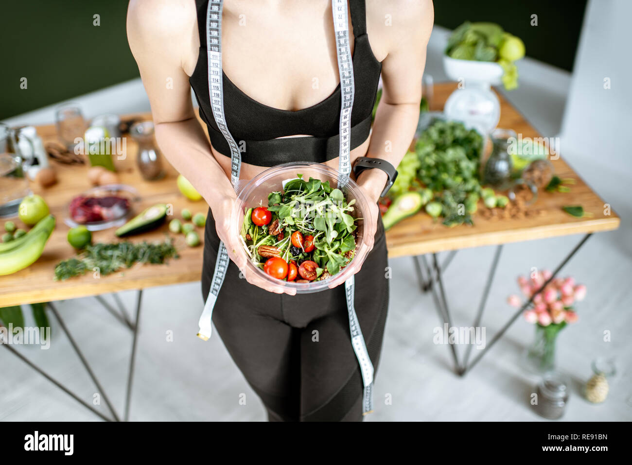 Athletic woman in sportswear holding salad near the table full of healthy products. Healthy eating and sports lifestyle concept Stock Photo