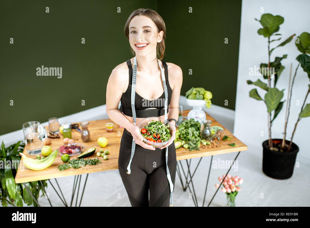 Happy woman in sportswear holding salad near the table full of healthy products. Healthy eating and sports lifestyle concept Stock Photo