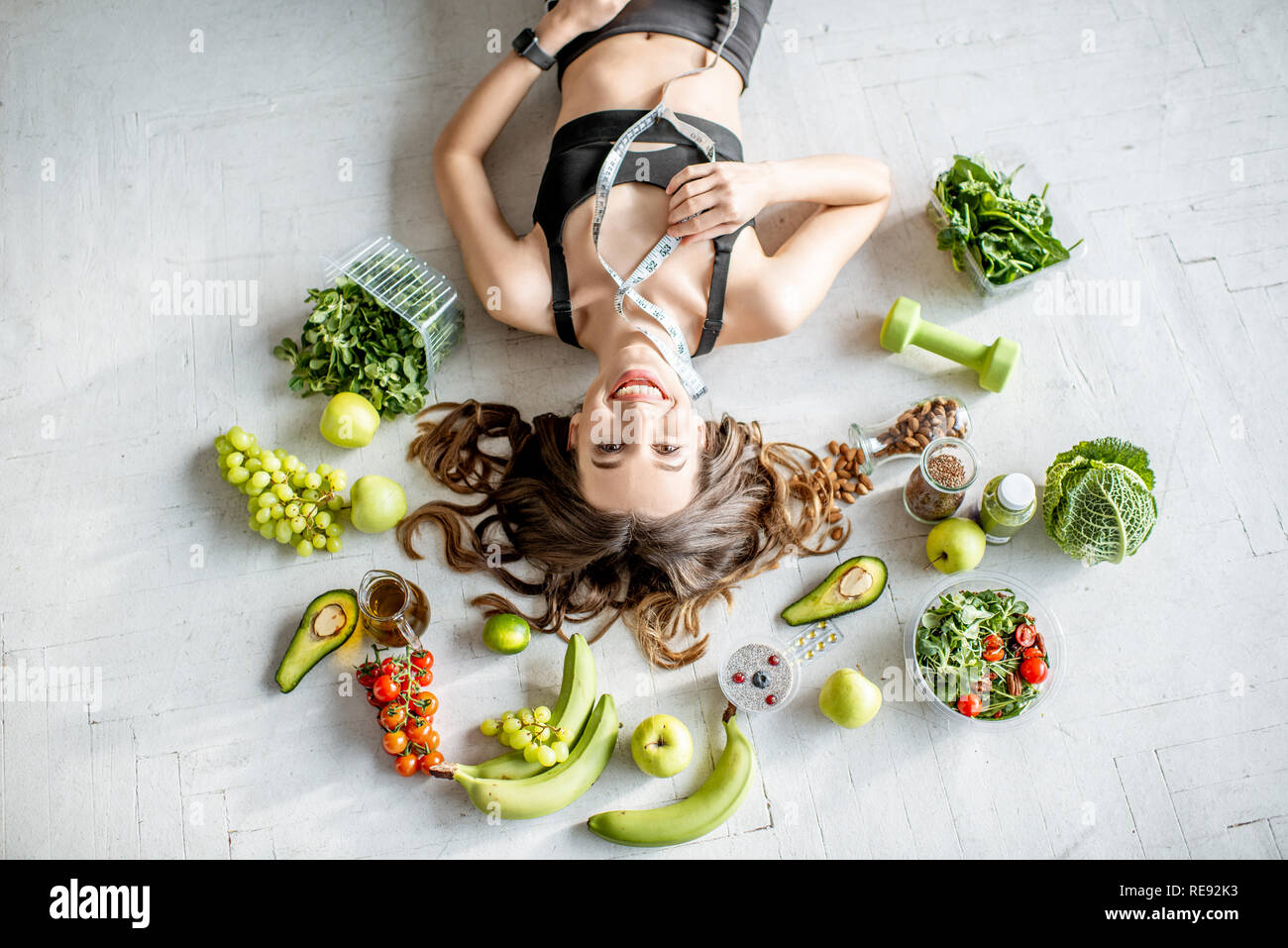 Beauty portrait of a sports woman surrounded by various healthy food lying on the floor. Healthy eating and sports lifestyle concept Stock Photo