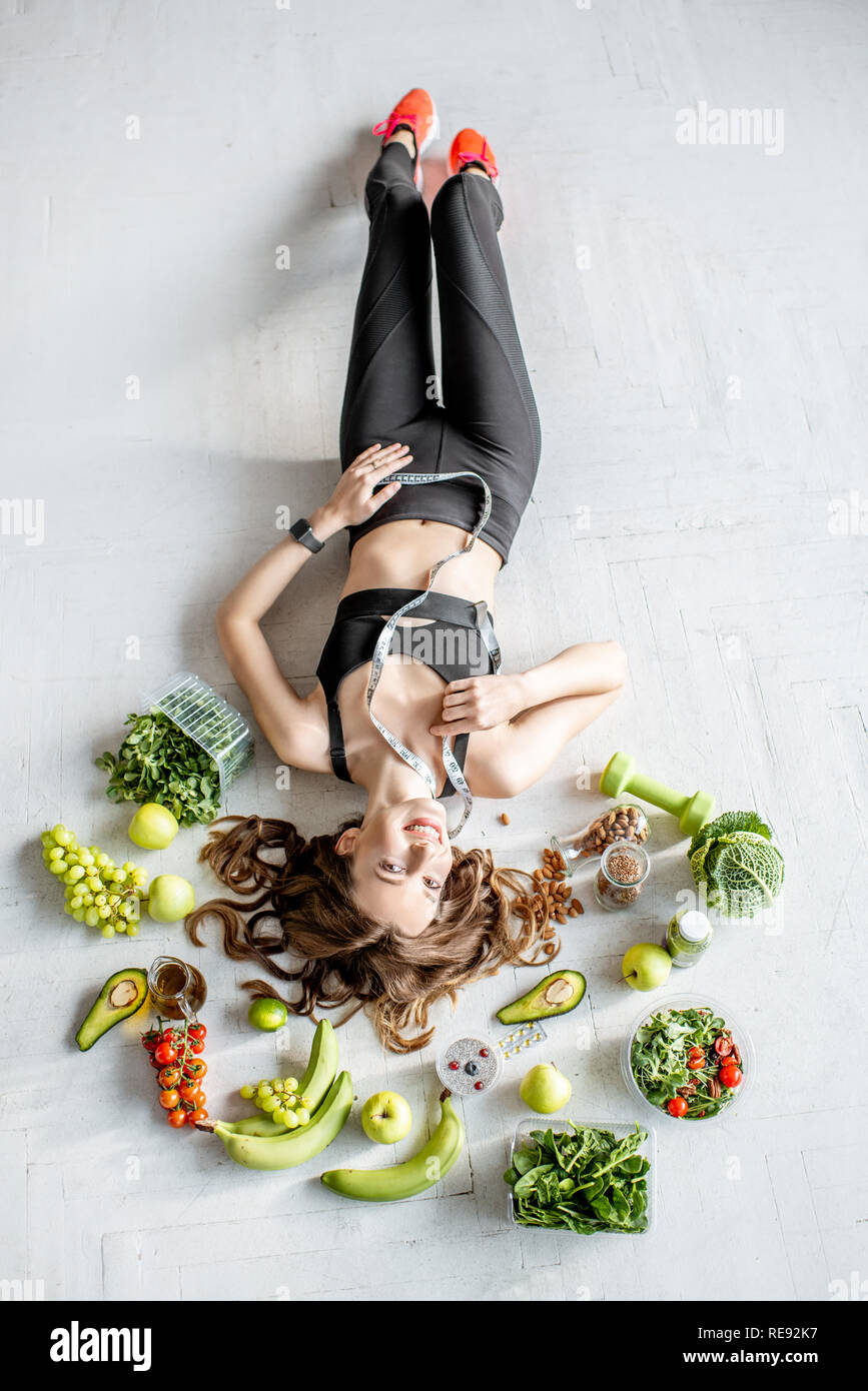 Full body portrait of a sports woman surrounded by various healthy food lying on the floor. Healthy eating and sports lifestyle concept Stock Photo
