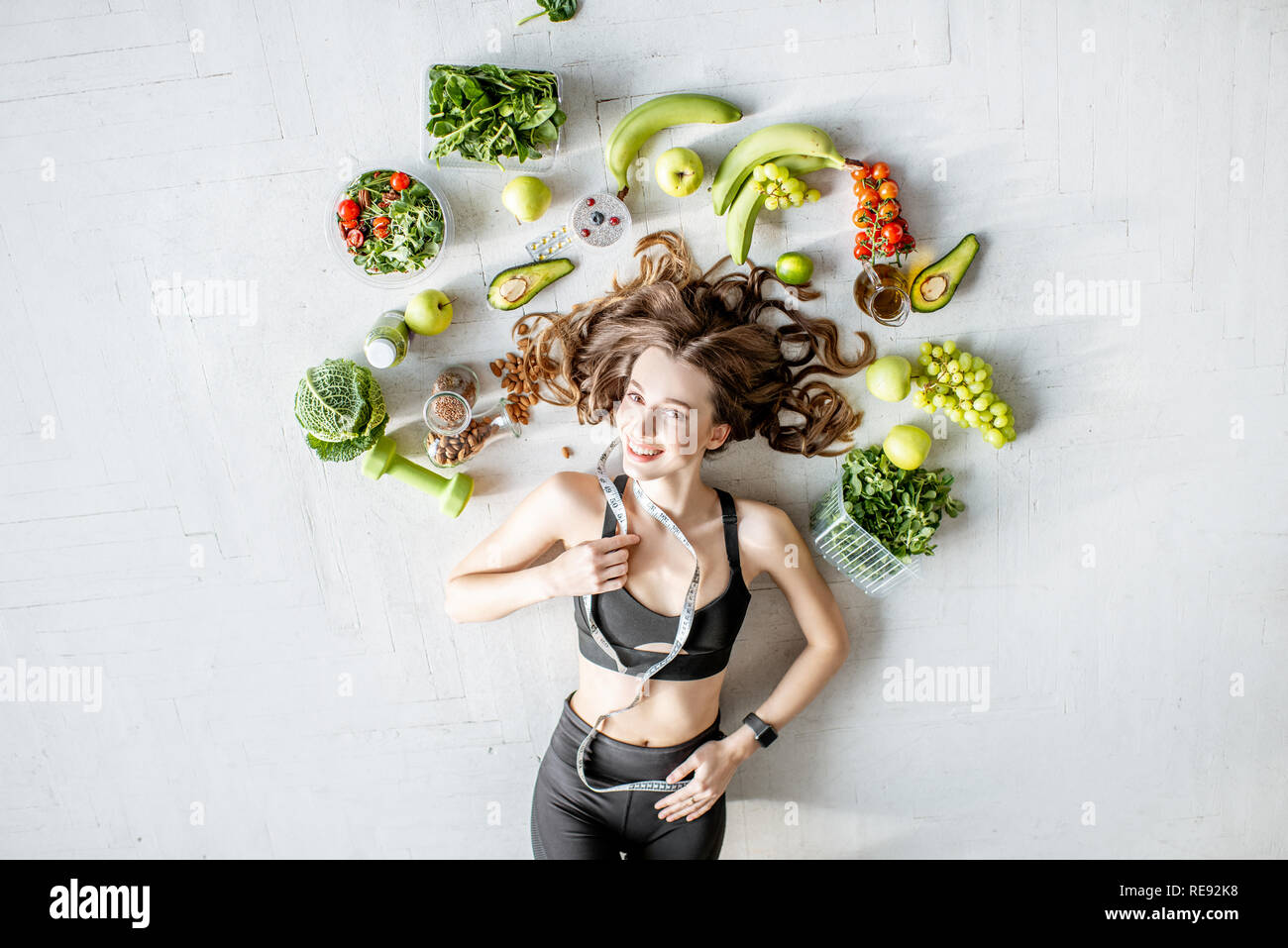 Beauty portrait of a sports woman surrounded by various healthy food lying on the floor. Healthy eating and sports lifestyle concept Stock Photo