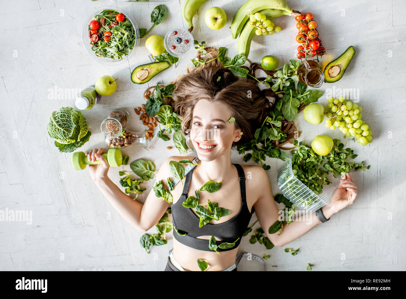 Beauty portrait of a sports woman surrounded by various healthy food lying on the floor. Healthy eating and sports lifestyle concept Stock Photo