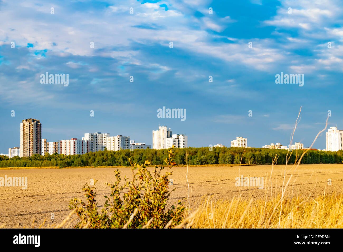 View over a harvested field to the satellite city Gropiusstadt in Berlin-Neukoelln illuminated by the sun. Stock Photo