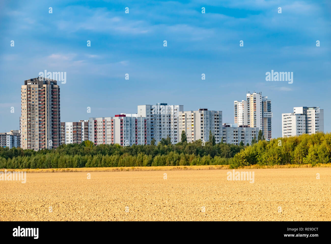 View over a harvested field to the satellite city Gropiusstadt in Berlin-Neukoelln illuminated by the sun. Stock Photo