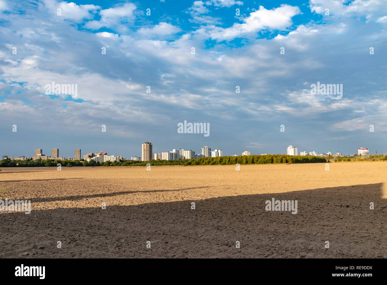 View over a harvested field to the satellite city Gropiusstadt in Berlin-Neukoelln illuminated by the sun. Stock Photo