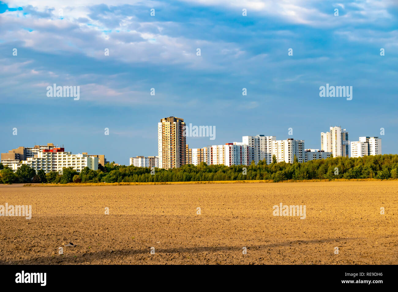 View over a harvested field to the satellite city Gropiusstadt in Berlin-Neukoelln illuminated by the sun. Stock Photo