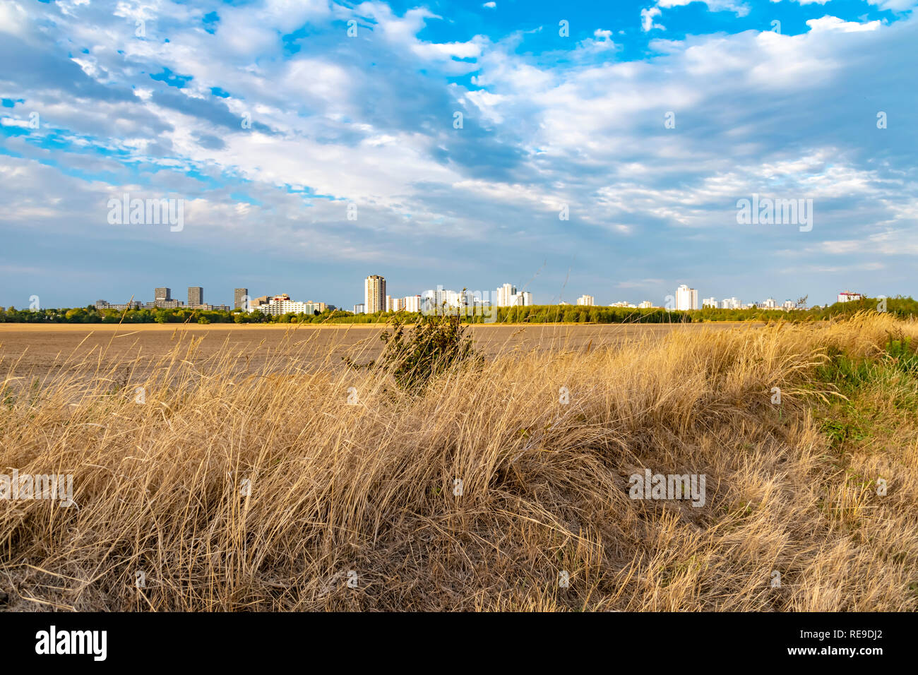 View over a harvested field to the satellite city Gropiusstadt in Berlin-Neukoelln illuminated by the sun. Stock Photo