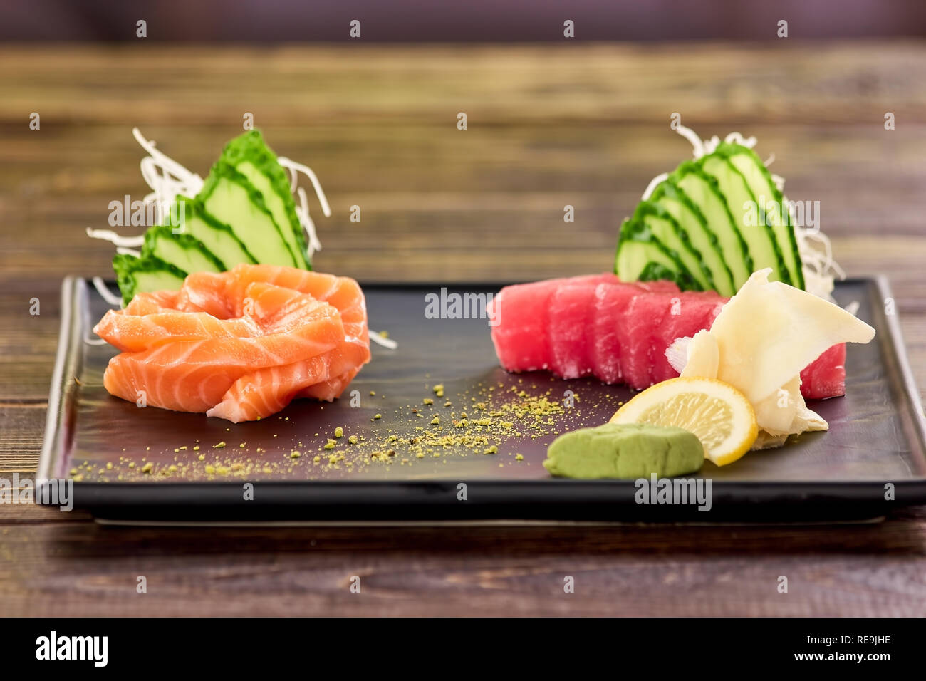 Sliced red and orange fish fillet and side dish. Salmon, tuna, cucumber slices, white ginger, wasabi and lemon. Stock Photo