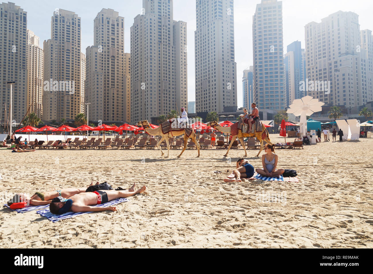 DUBAI, UAE - January 07, 2019: Camels and lying tourists on skyscrapers background at the beach Stock Photo