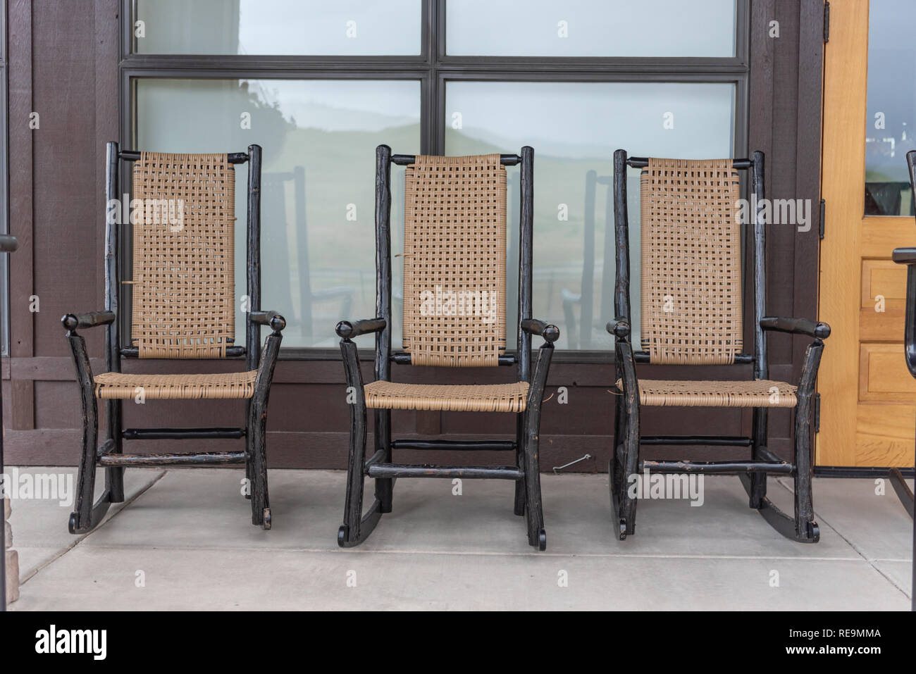 Three Wood and Wicker Rocking Chairs in front of Building Stock Photo