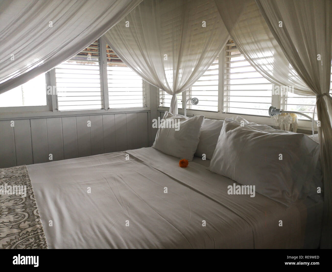 Pillows on a white canopy bed with curtains, light coming in from the