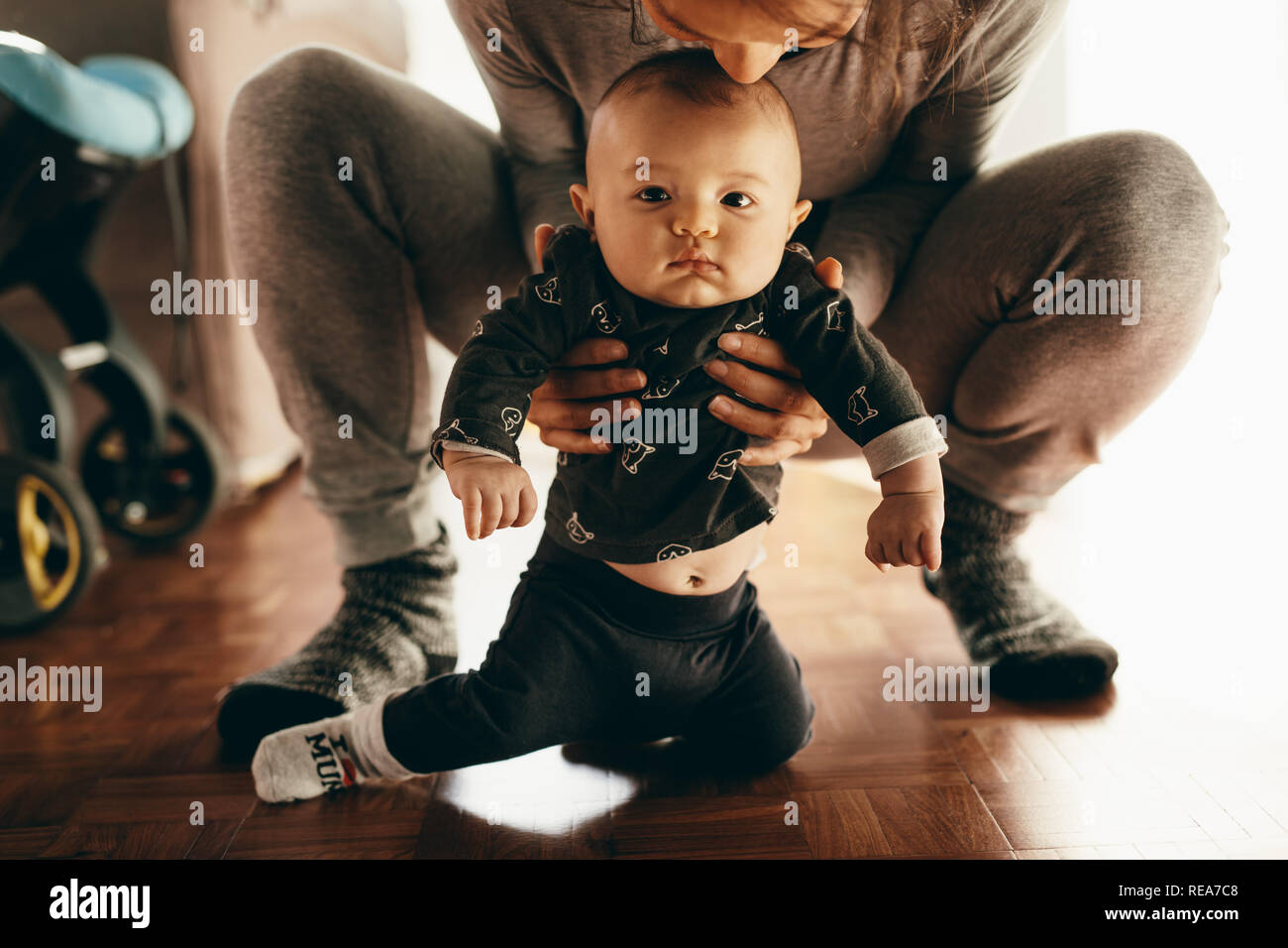 Close up of a mother playing with her son at home. Woman squatting and holding her baby from behind at home. Stock Photo