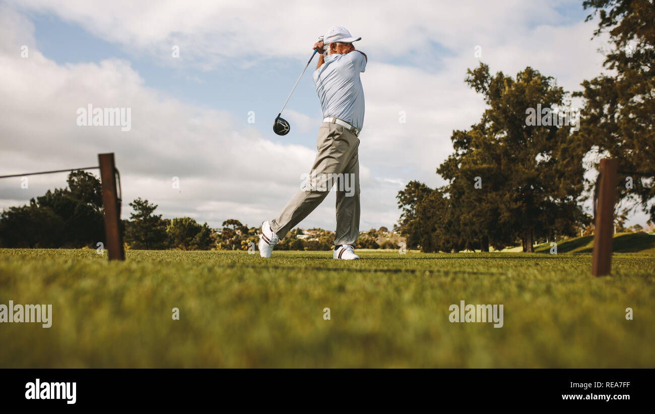 Professional golfer taking shot on the golf course. Senior golf player swinging golf club on the green. Stock Photo