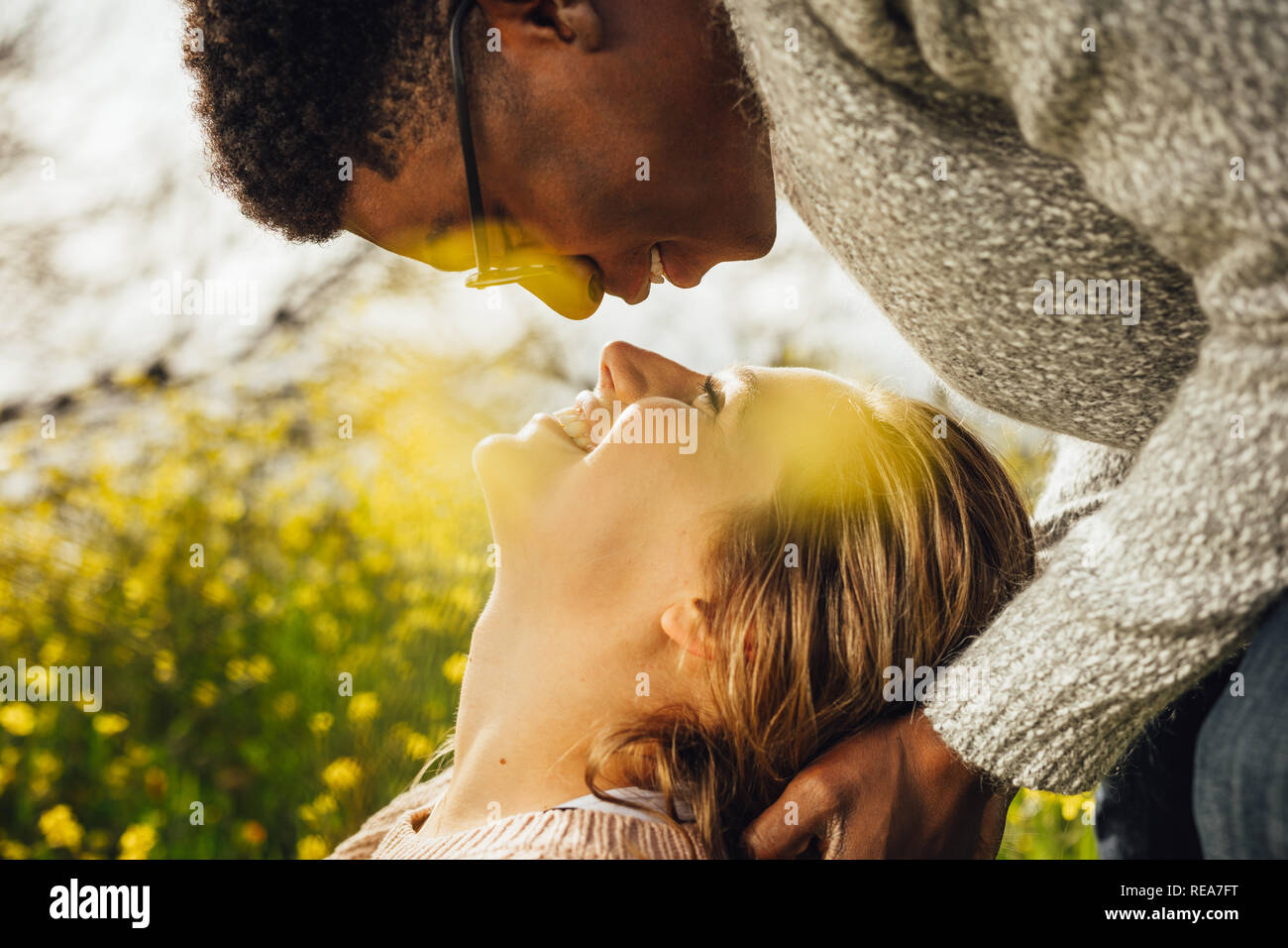 Close up of young man and woman looking at each other with love. Interracial couple outdoors in meadow. Stock Photo