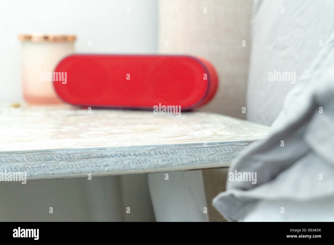 Bright red radio alarm clock and candle jar on a bedside table nightstand, with bed and linens showing in soft colors. Stock Photo