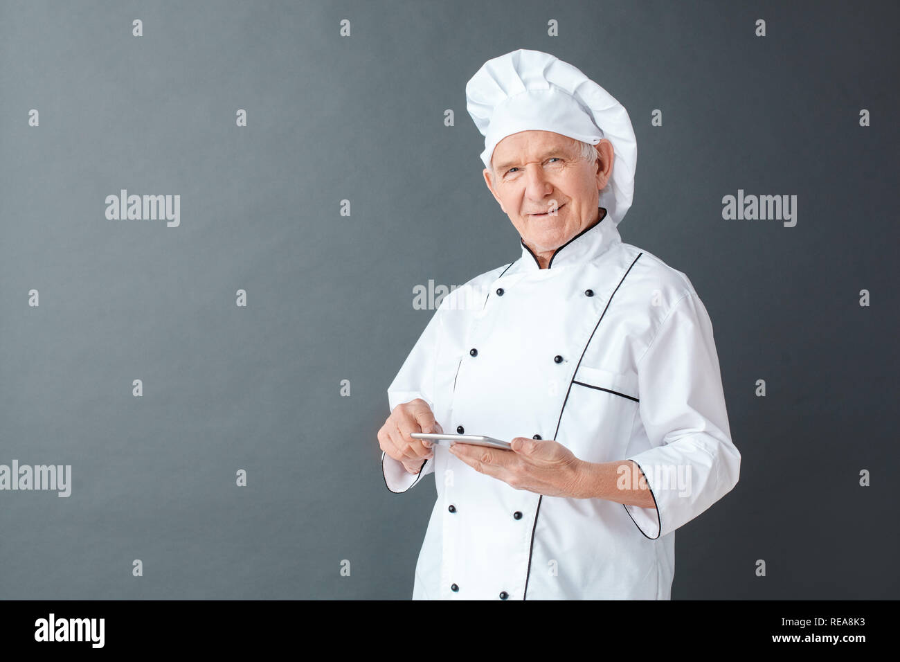 Senior chef studio standing isolated on gray with digital tablet ...
