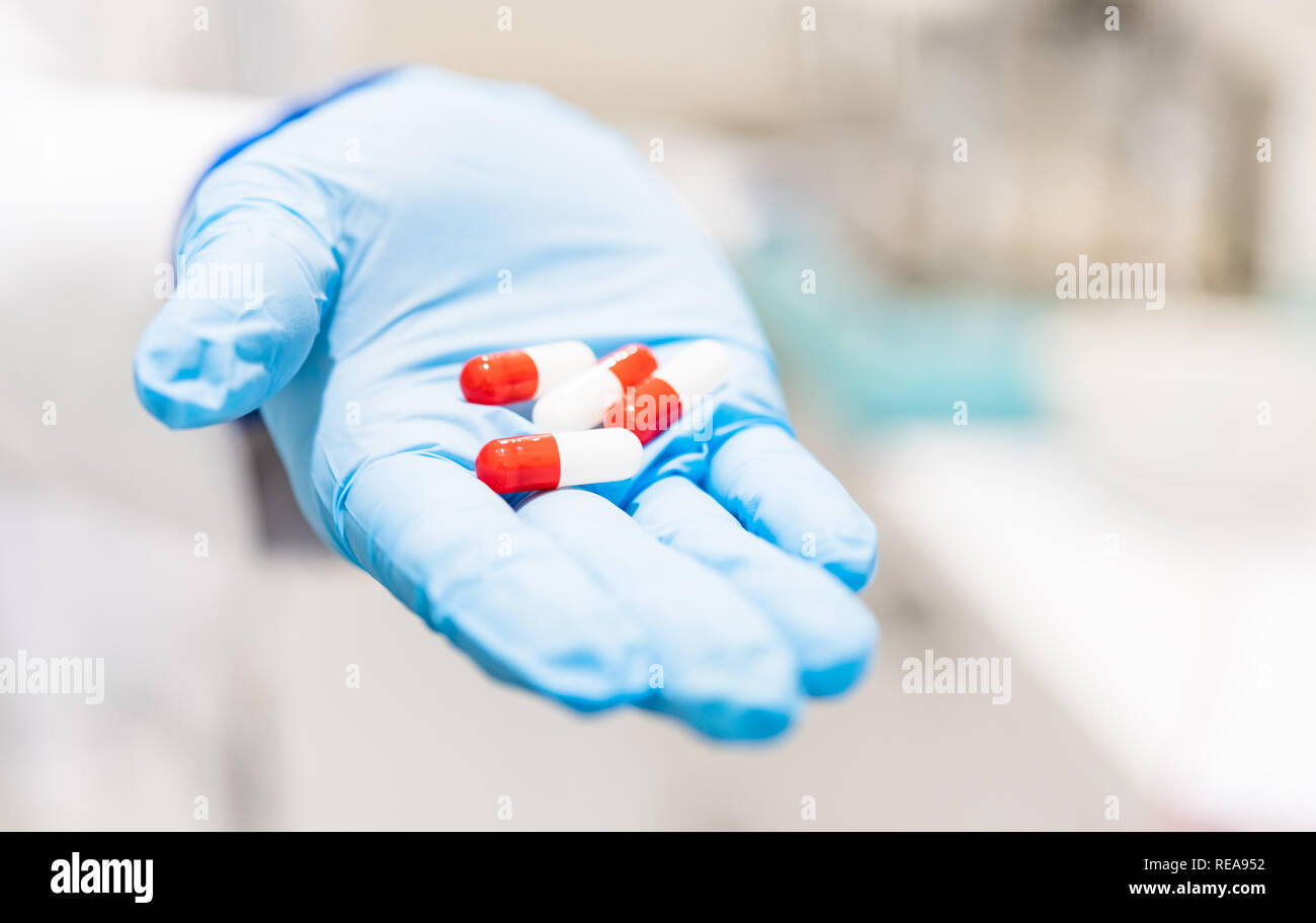 Detail of human hands with glove holding group of red pills in pharmacy laboratory Stock Photo