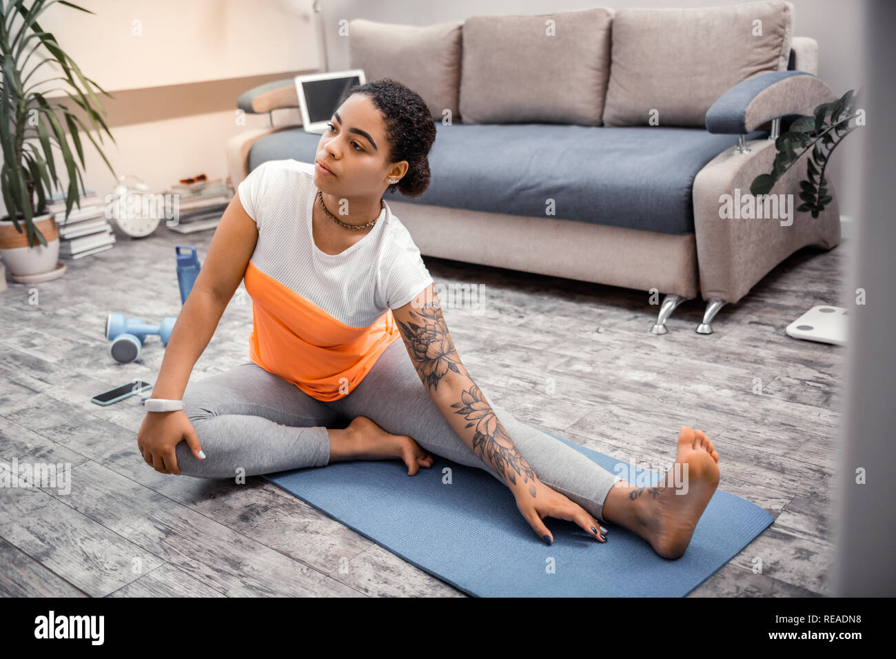 Serious dark-haired woman sitting on blue mat during taking exercises Stock Photo