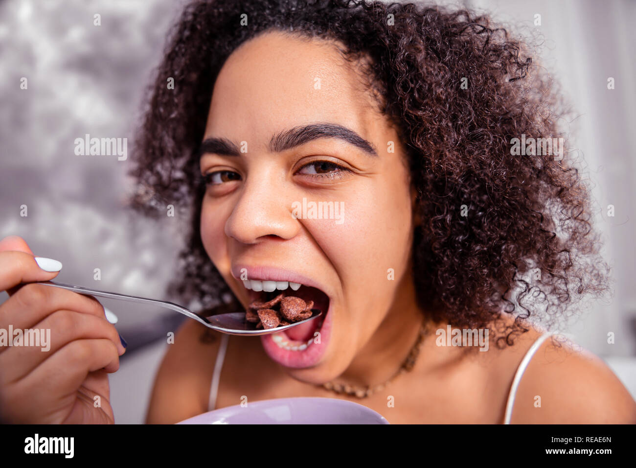 Attractive darkhaired lady throwing chocolate cereals in her open