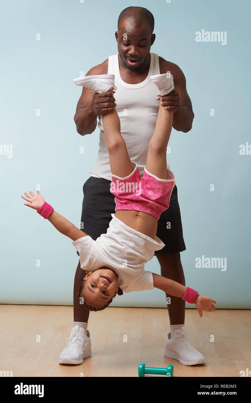 Handsome black young father is holding his cute little daughter upside down at home. She enjoys it big time, swinging from side to side. Stock Photo