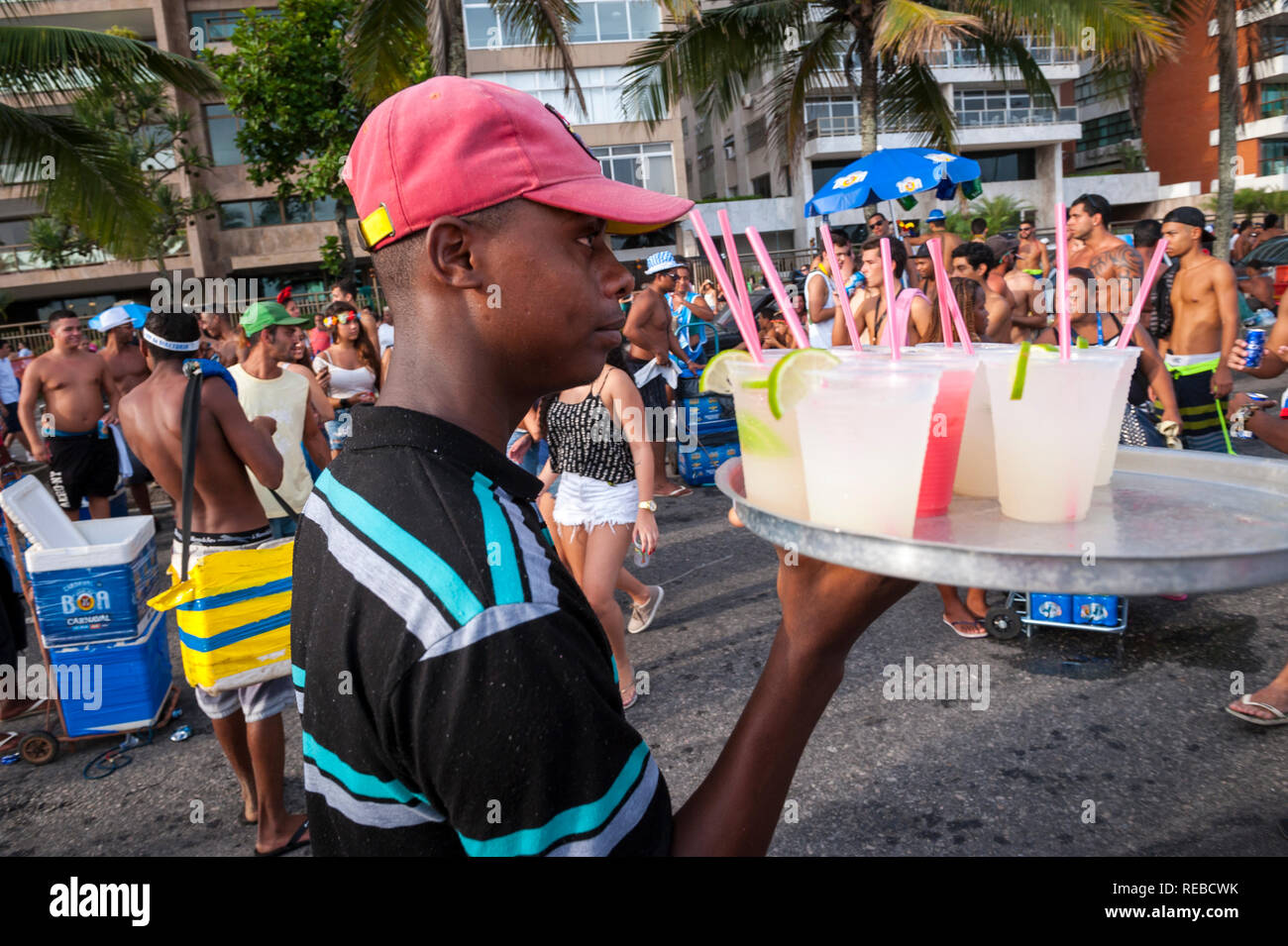 RIO DE JANEIRO - MARCH 15, 2017: An unlicensed young Brazilian vendor carries homemade caipirinha cocktails on a tray through the crowd at a Carnival Stock Photo