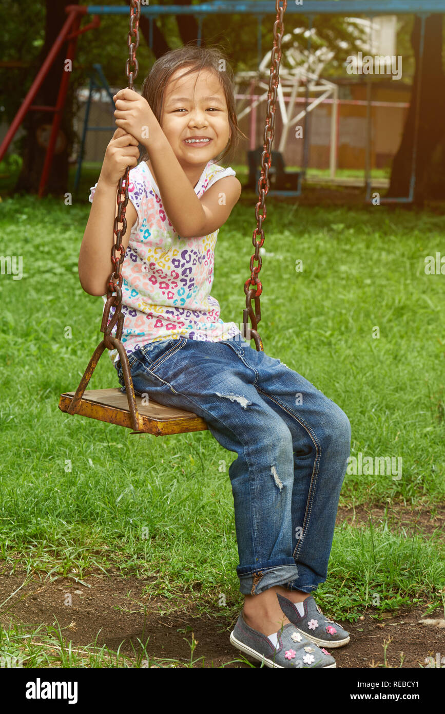 Portrait of active asian girl sitting in park swings Stock Photo
