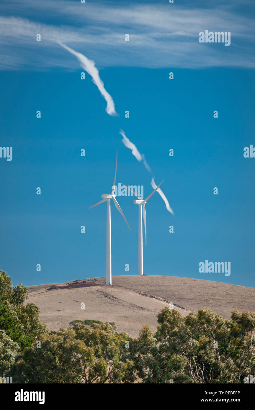 Two wind turbines following a hill line against a blue sky with clouds ...