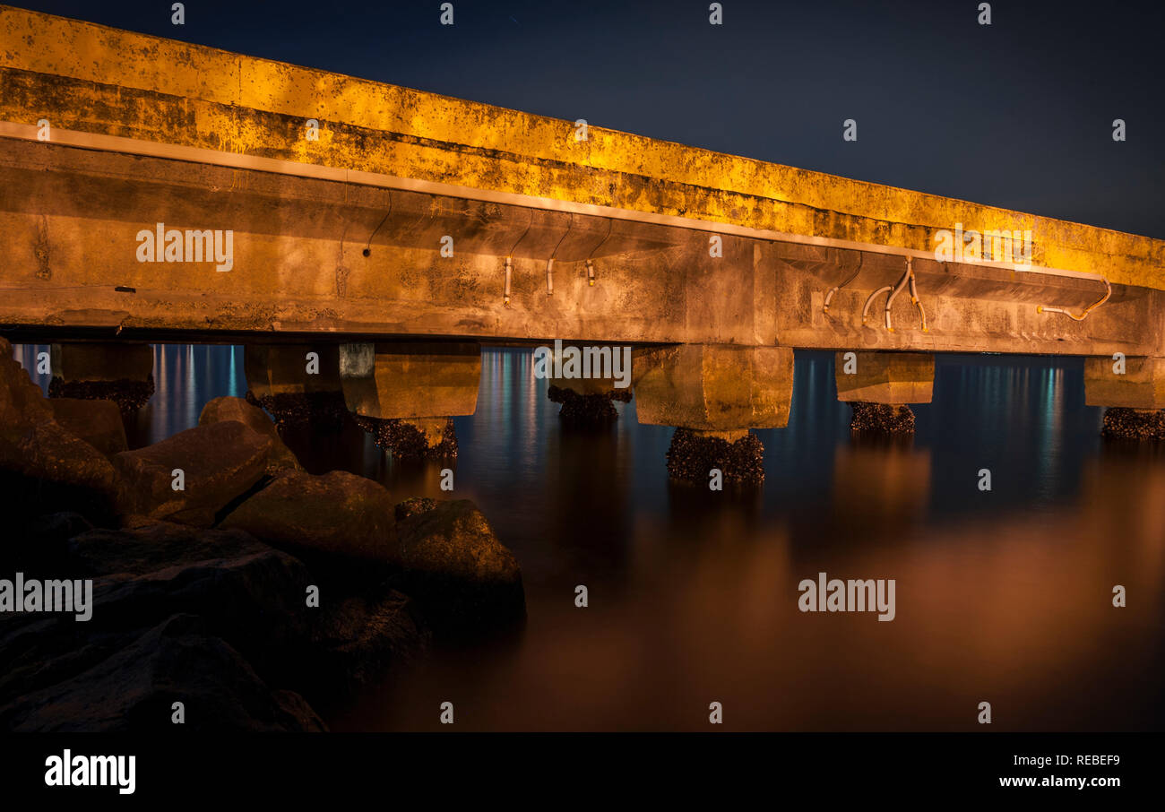 A concrete pier at night, long exposure with water in motion and orange light Stock Photo