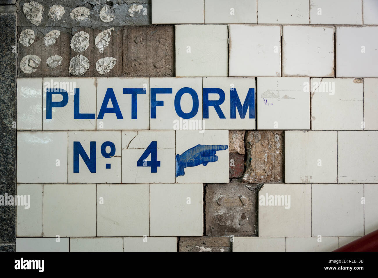 Platform No. 4 with a pointing finger icon and a wall with broken and missing tiles, blue on white Stock Photo