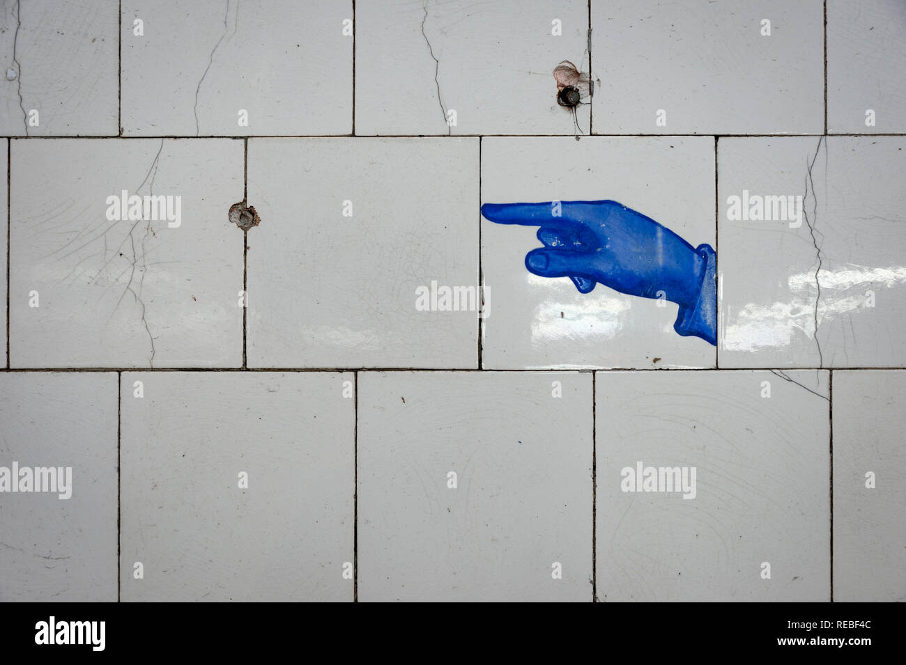 A painted pointing finger icon on old white subway tiles in a train station, blue against white Stock Photo