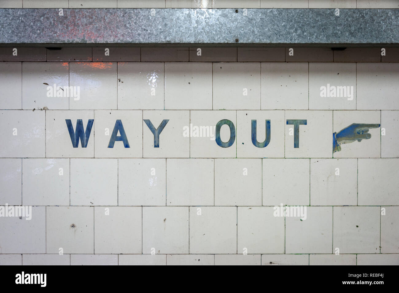 Old Way Out sign with hand pointing finger on old white tiles in train station Stock Photo