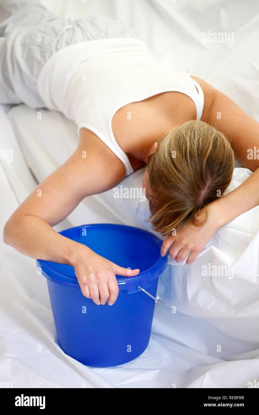 Woman is vomiting into a bucket, nausea, sickness Stock Photo