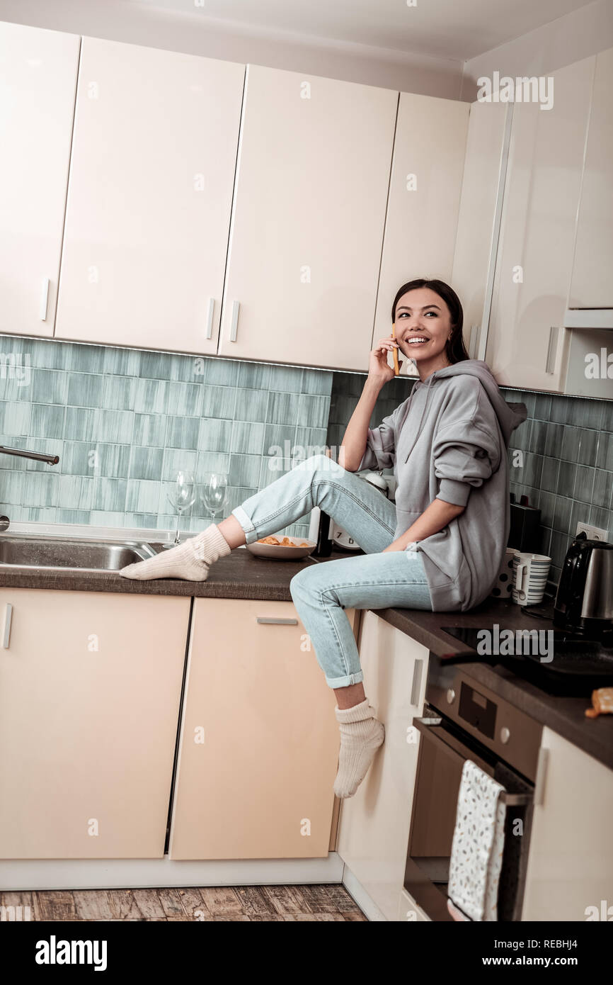 Dark-haired woman wearing jeans and warm socks sitting in the kitchen ...