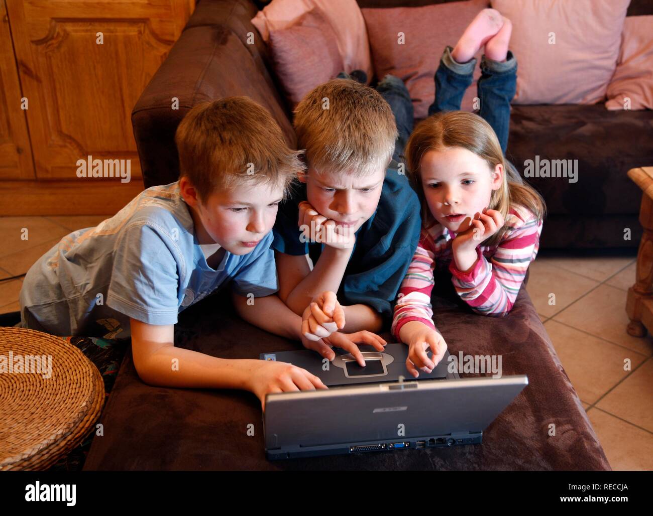 Siblings, 7, 11, 13 years old, with laptop computer, in the living room