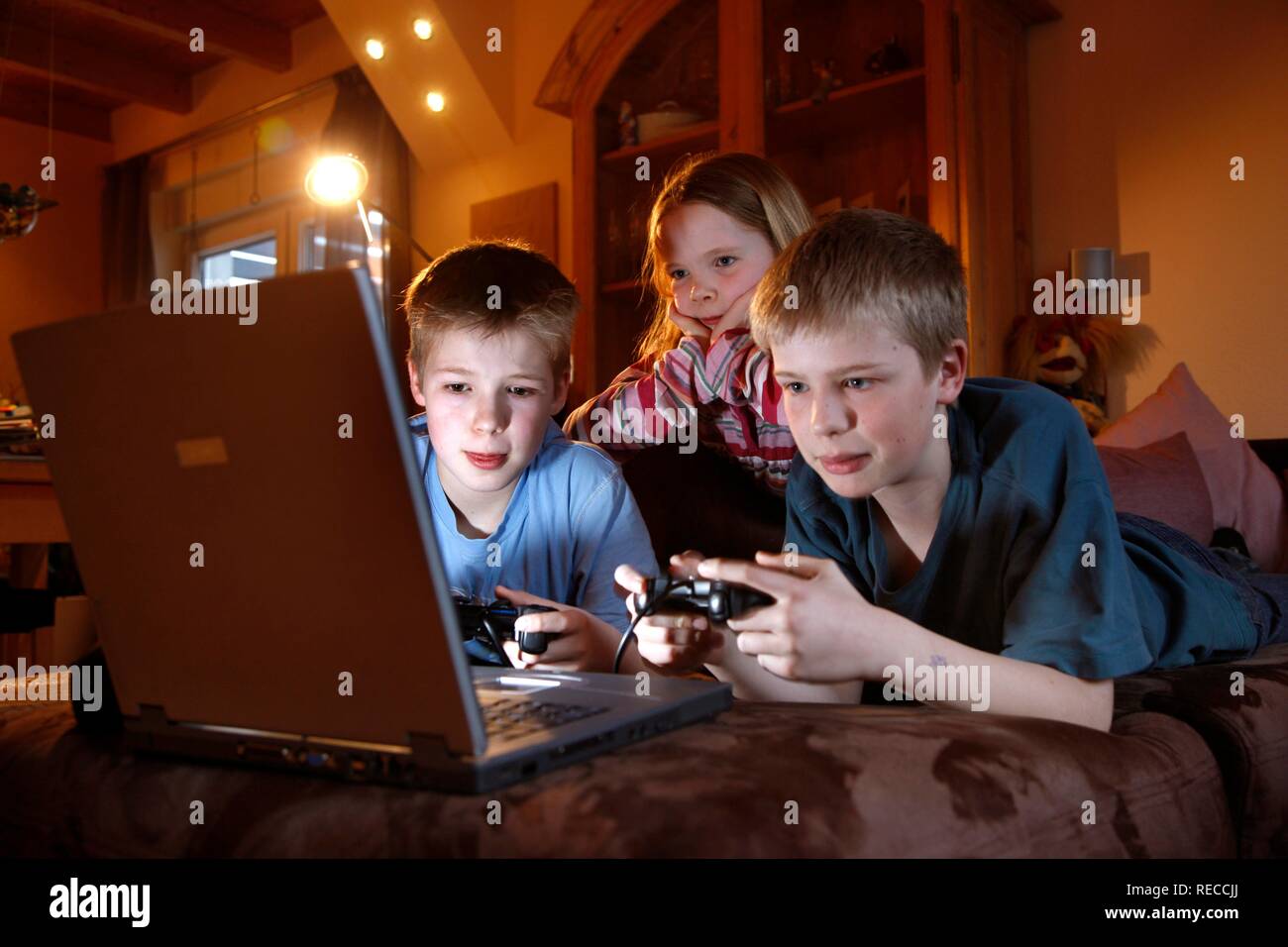Siblings, 7, 11, 13 years old, with laptop computer in the living room, playing a car racing computer game Stock Photo