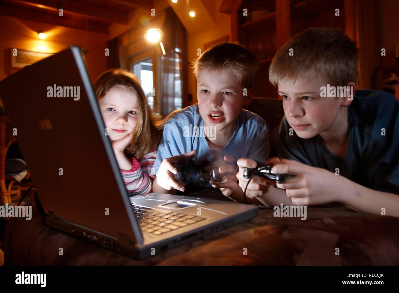 Siblings, 7, 11, 13 years old, with laptop computer in the living room, playing a car racing computer game Stock Photo