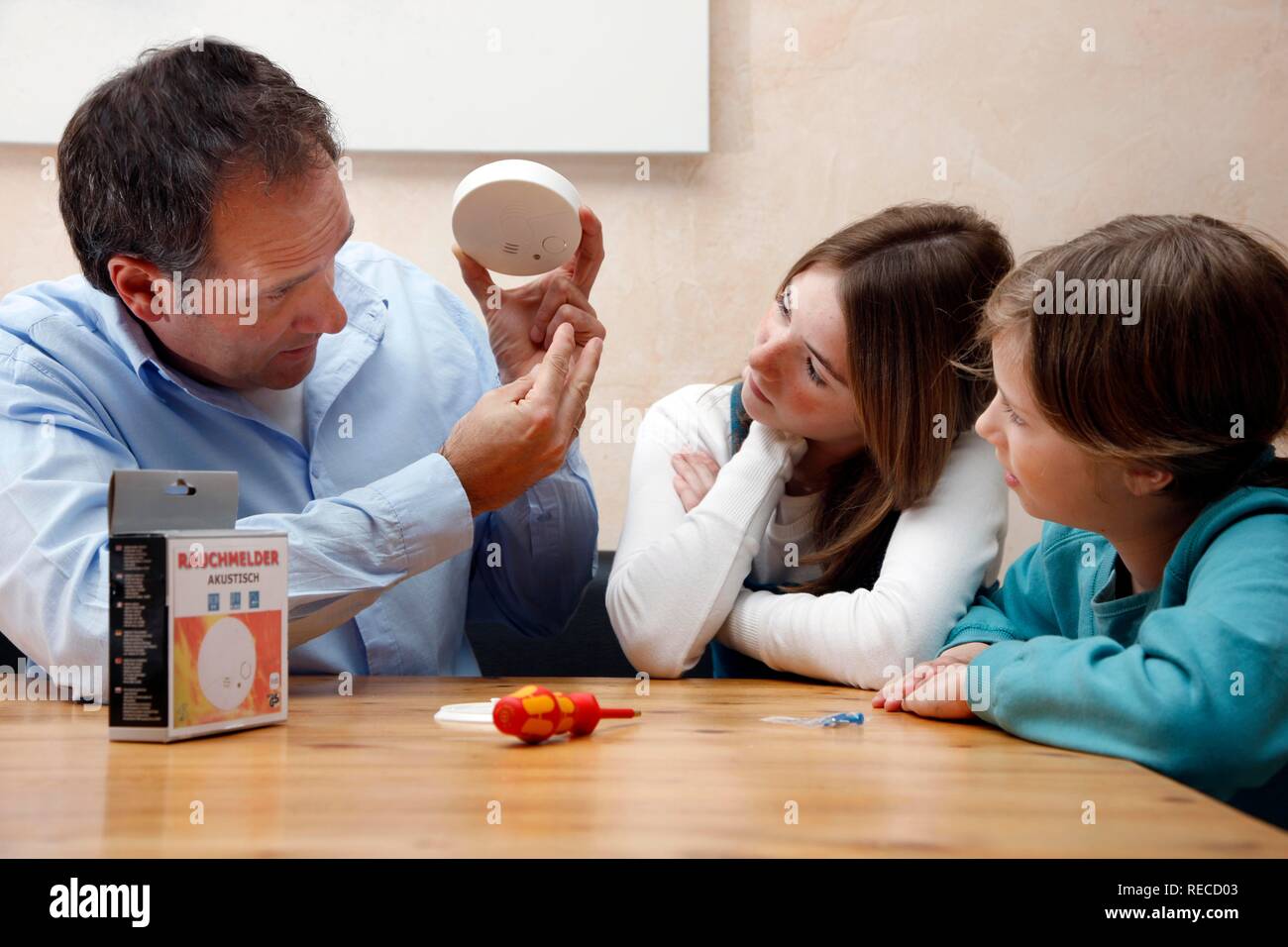 A father explaining the significance and function of a smoke detector in a private home to his daughters Stock Photo