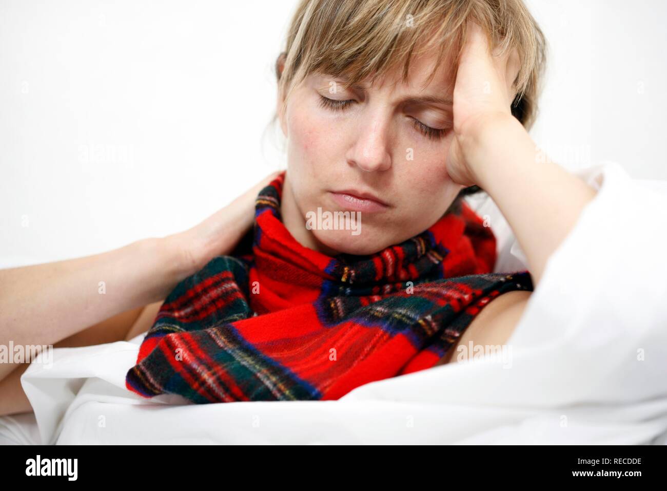 A young woman with a sore throat and a cold in bed, with a scarf Stock