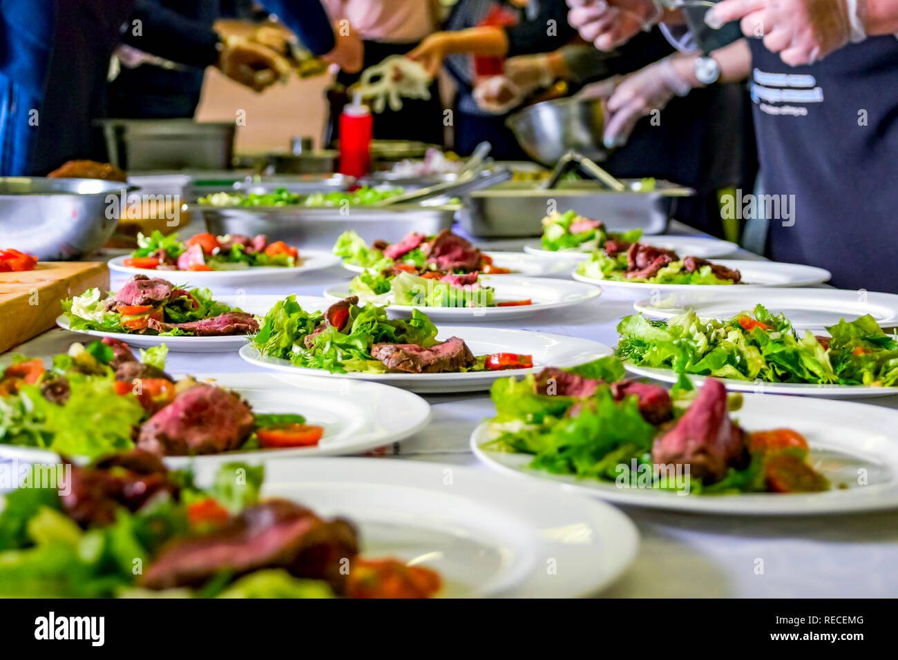 Cooked Roast Beef, Fresh Salad And Tomatoes Served On White Plates. Cooking Master Class, Workshop with People Learning How to Cook Around the Table Stock Photo