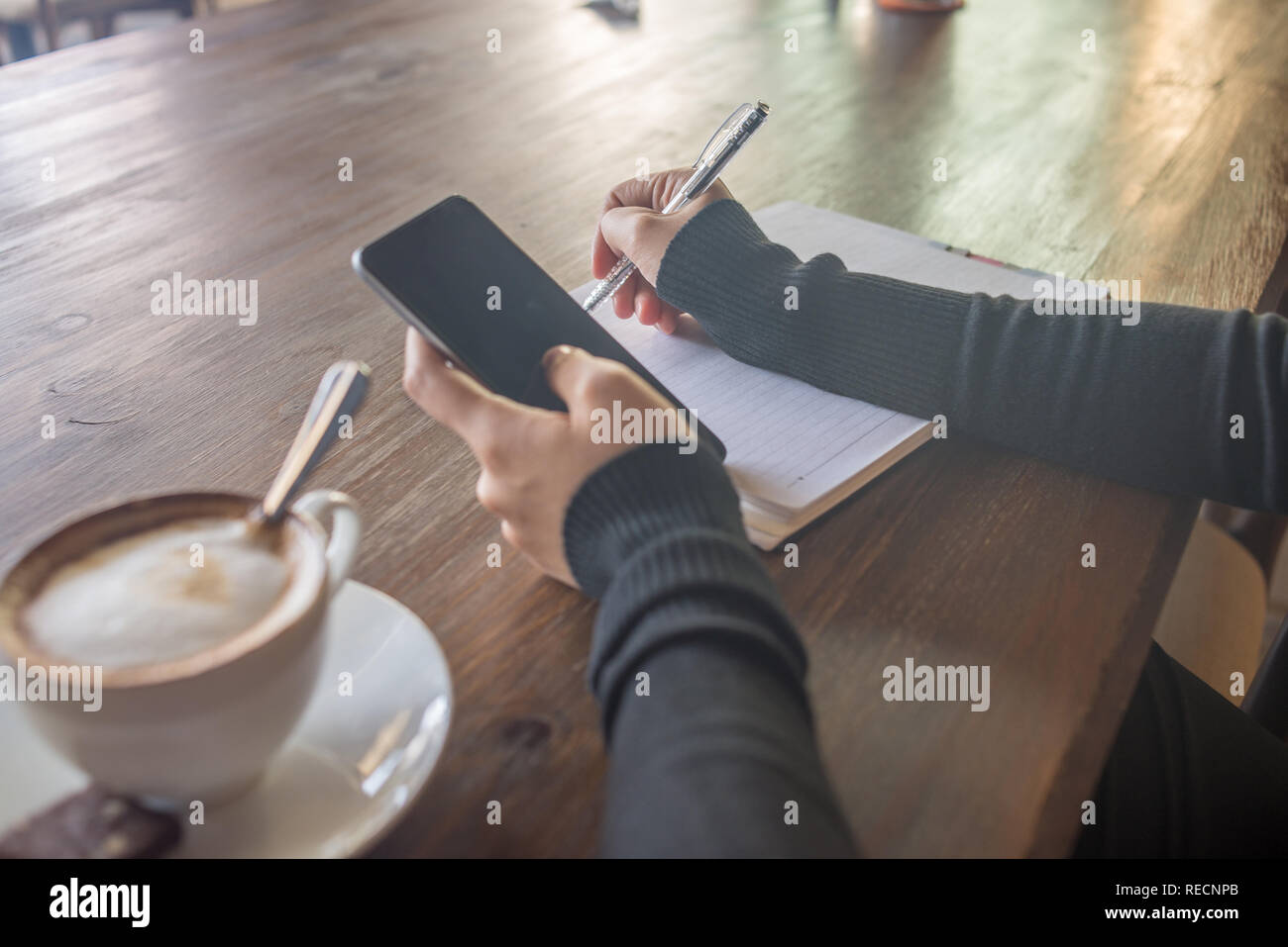 Woman hand using smartphone and writing notes Stock Photo