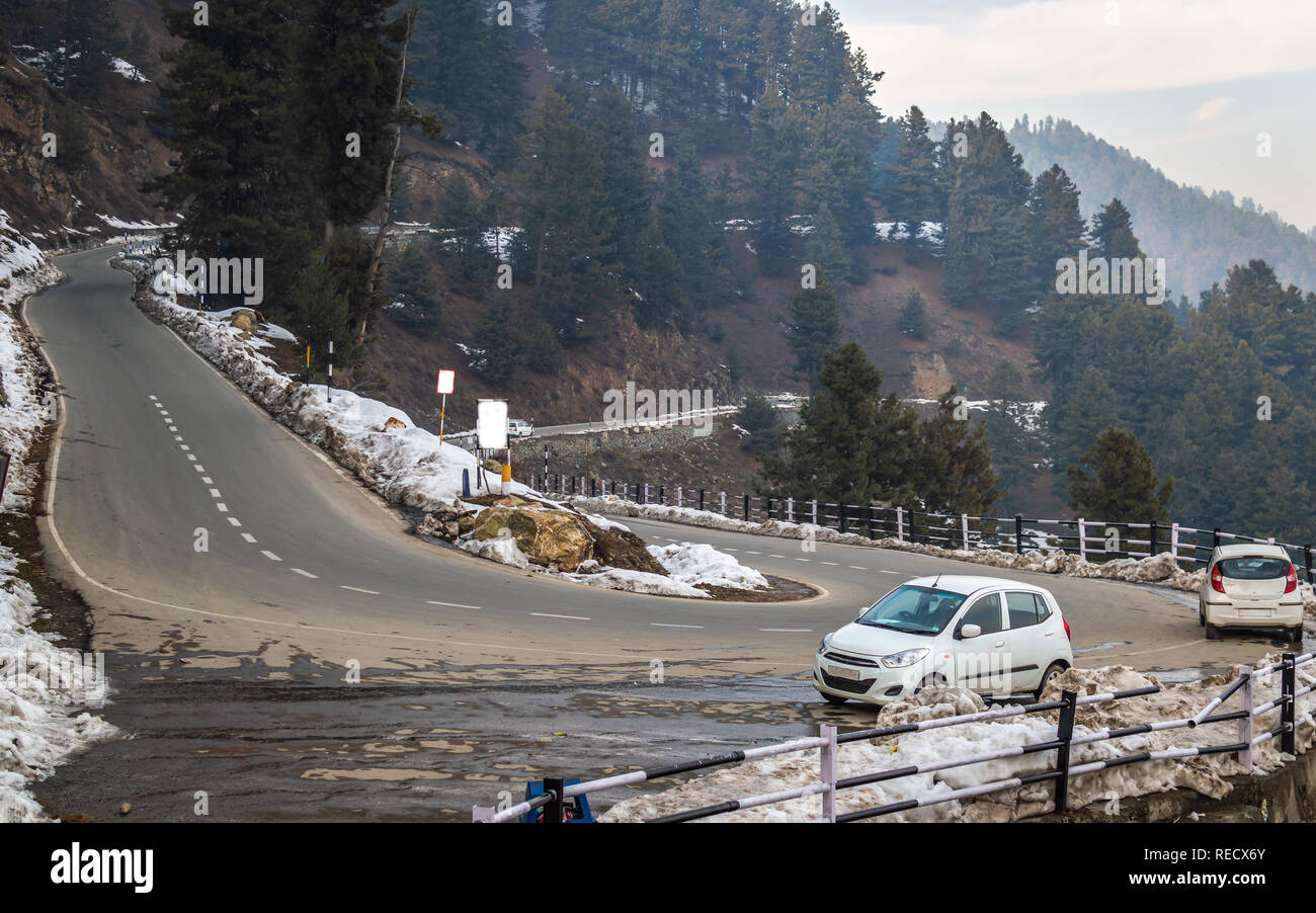 Gulmarg, Jammu and Kashmir, India: Date- November 15, 2018- Snow along the sides of curvy roads on hilly terrain with cars parked Stock Photo