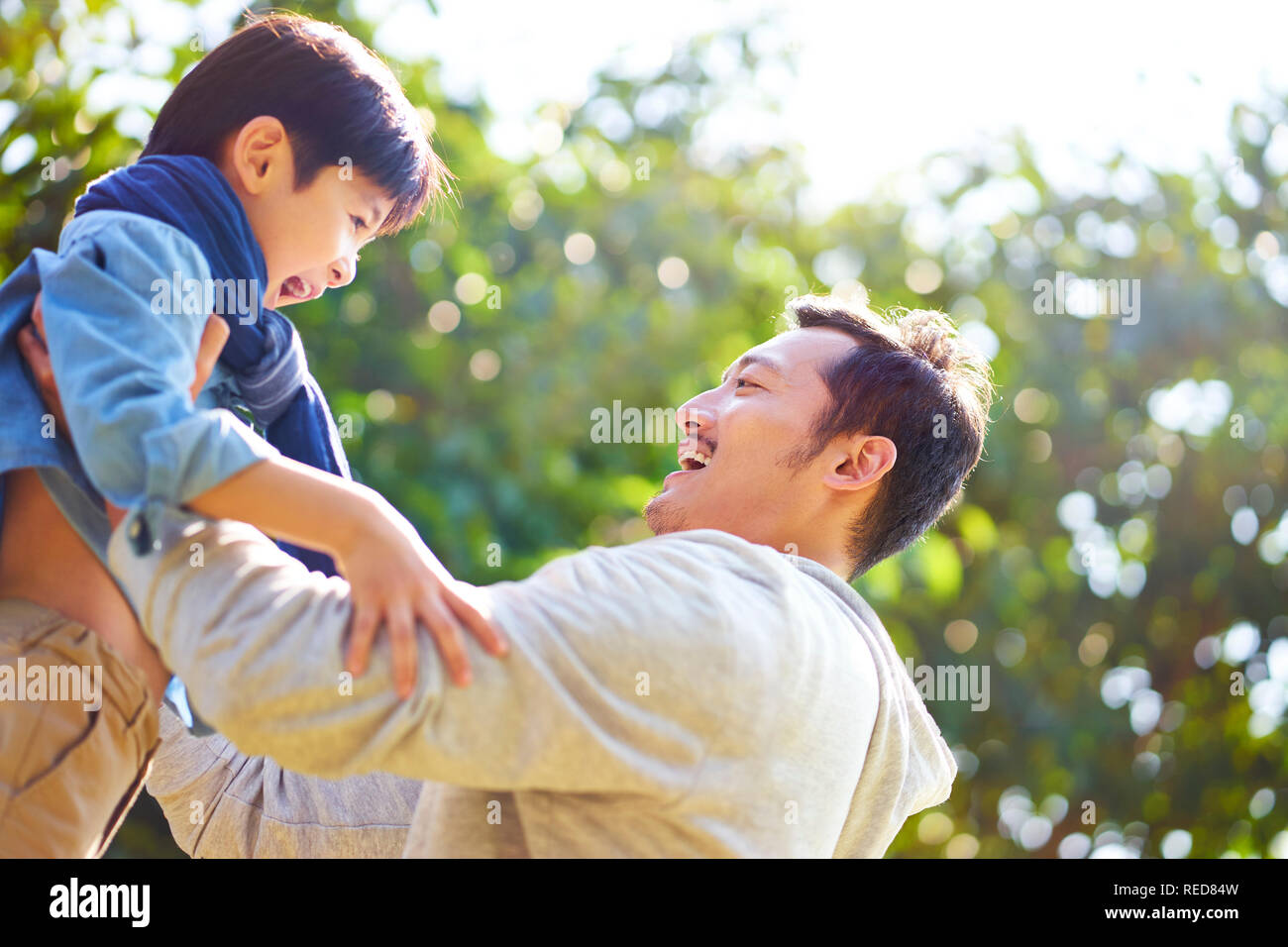 asian father having fun lifting son oudoors in park. Stock Photo