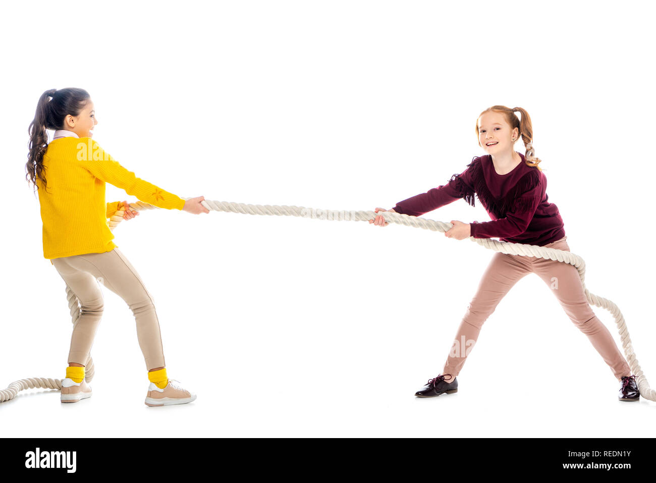 two cheerful schoolgirls pulling rope isolated on white Stock Photo